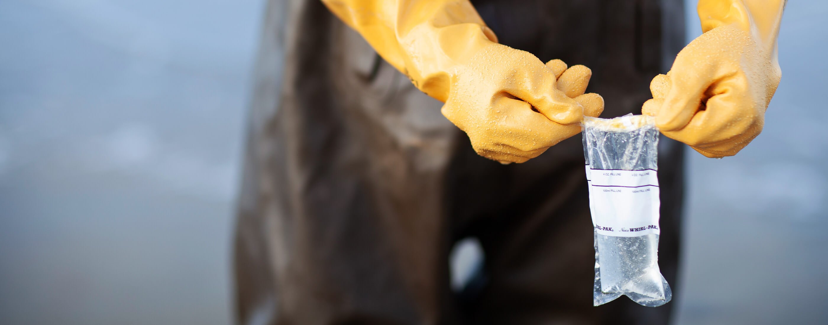 Volunteer holding up water sample wearing yellow gloves